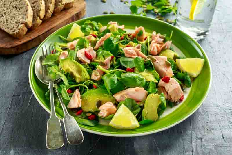 Healthy Salmon, Avocado salad with watercress and goji berries, pumpkin seed mix on green plate