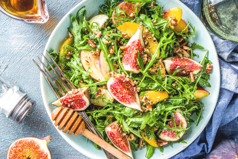 Homemade salad bowl with figs, arugula, peach and apple slices, nuts and honey.