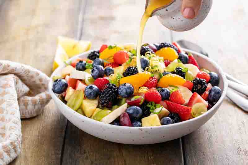 Fruit salad on a wooden table with berries, citrus zest, with mint and honey dressing pouring over