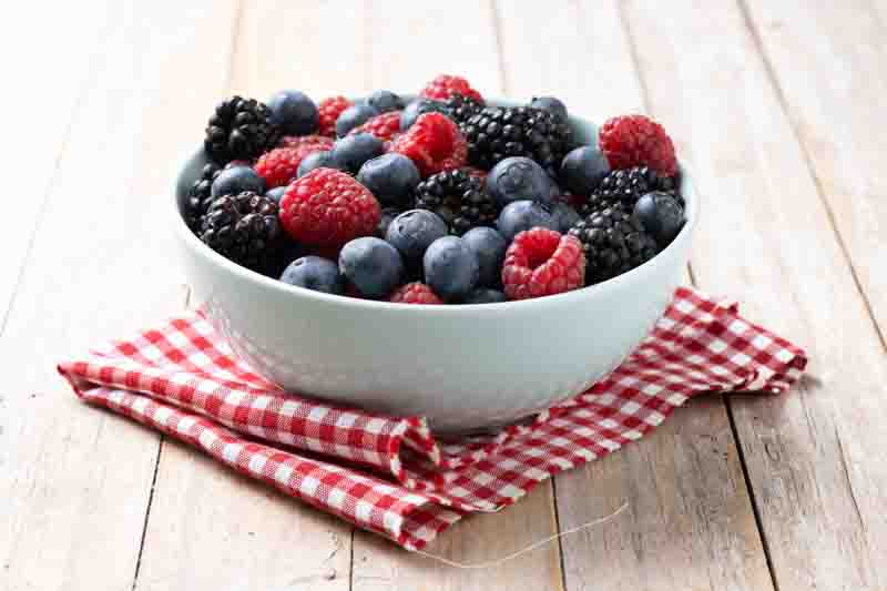 Fresh assortment berries in bowl on wooden table.