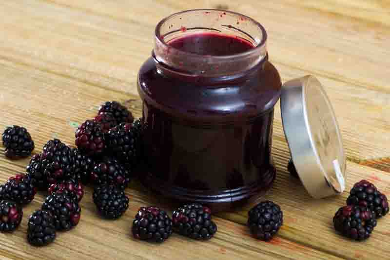 Healthy vitamin dessert. Ripe berries of fresh sweet blackberry and jar of jam on wooden table..