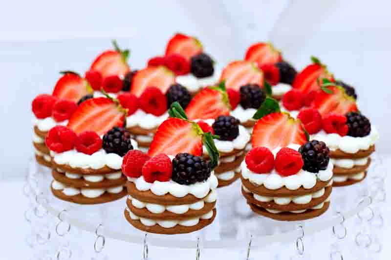 Desserts decorated with strawberries, raspberries, blackberries are arranged on clear stand for special event.