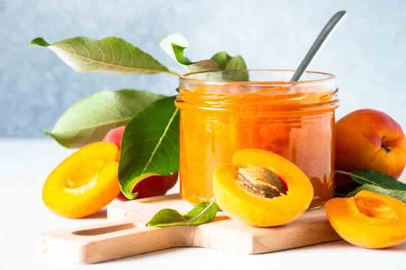 Apricot jam in glass jar at white table.