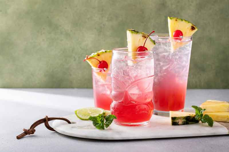 Singapore sling cocktail in variety of glasses garnished with pineapple and cherry with copy space