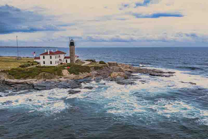 Aerial view of a picturesque Beavertail lighthouse on a rocky coastline with waves crashing, Newport, Rhode Island