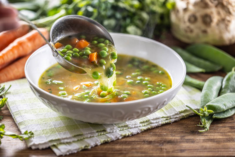 Healthy vegetable soup from fresh spring vegetables. Scooping up hot soup with a ladle.