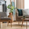 Real photo of an armchair with a book standing next to a small table with pot and sofa with cushions in cozy living room interior with plants