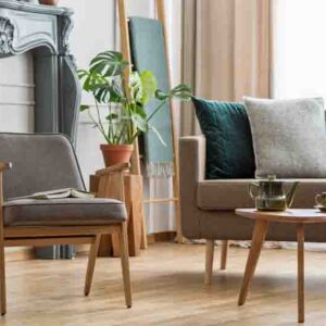 Real photo of an armchair with a book standing next to a small table with pot and sofa with cushions in cozy living room interior with plants