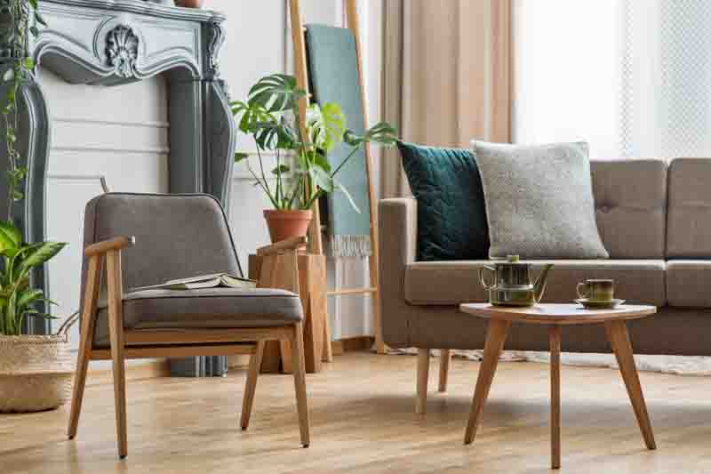 Real photo of an armchair with a book standing next to a small table with pot and sofa with cushions in cozy living room interior with plants