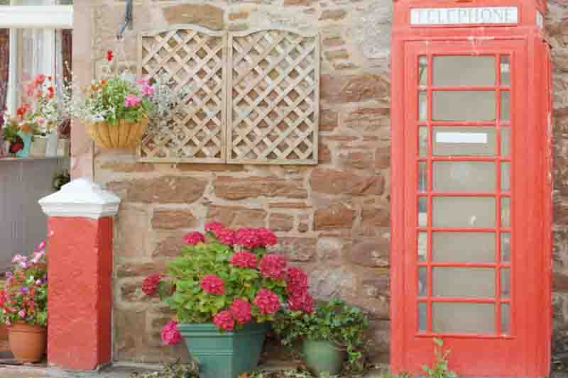 A classic red telephone box stands beside a stone wall with vibrant potted hydrangea flowers.